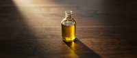 Bottle of golden oil on wooden surface with warm sunlight casting dramatic shadows, suitable for culinary, wellness, and product marketing applications.