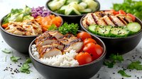 Grilled chicken and rice bowls with fresh vegetables, avocado, and cherry tomatoes served in black ceramic bowls. Healthy protein-rich meal prep for lunch.