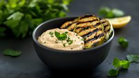 Creamy seafood dip with grilled mussels in black ceramic bowl, garnished with fresh herbs and lemon. Appetizing close-up on dark background.