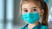 Young Caucasian girl wearing protective medical face mask and doctor costume with stethoscope, looking at camera in hospital setting, healthcare concept.