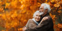 Happy senior couple embracing in autumn park with golden foliage, elderly man and woman showing love and affection outdoors during fall season.