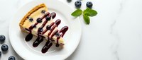 Delicious cheesecake slice with fresh blueberries and chocolate drizzle on white plate, garnished with mint leaves for dessert presentation.
