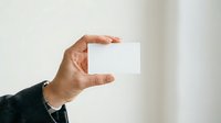 Adult male hand holding blank white business card against neutral background for branding and corporate identity mockup purposes.