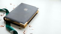 Elegant gray hardcover book with golden edges and embossed logo on white surface with green ribbon and scattered rose petals for luxury branding design.