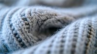 Soft knitted wool texture in light blue and gray tones with ribbed pattern detail, showing cozy winter fabric structure in macro photography.
