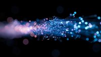 Glowing blue and pink particles with light trails creating dynamic motion effect against dark background, abstract digital network visualization for technology designs.