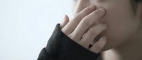 Young woman cupping hand to ear in listening gesture wearing dark sweater against soft light background for communication and hearing concepts.