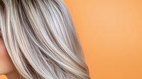 Young Caucasian woman with platinum blonde highlighted hair shown from side view against orange background, demonstrating professional hair coloring and styling technique.
