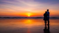 Romantic couple silhouette embracing on beach at golden sunset with ocean waves and colorful sky reflection on wet sand creating peaceful moment.