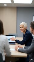 Confident mature businesswoman with short silver hair leading team meeting in modern office conference room discussing strategy and collaboration.