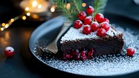 Chocolate cake slice dusted with powdered sugar and decorated with fresh cranberries and pine branch on dark plate, festive holiday dessert with bokeh lights.