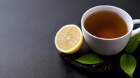 Hot tea with fresh lemon half and green citrus leaves on dark slate background. Copy space for text on left side. Healthy beverage concept.