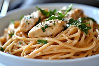 Creamy linguine pasta with tender chicken pieces, garnished with fresh herbs and black pepper in white ceramic bowl, appetizing close-up shot for menu or recipe.