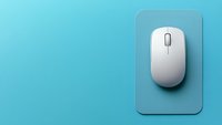 White wireless computer mouse on gray mousepad against turquoise blue background with copy space, minimalist office setup for business and technology concept.