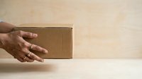 Male hand holding small cardboard box on neutral background. Suitable for shipping, delivery, e-commerce, packaging, logistics, and small business concepts.