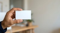 Man with dark skin tone holding blank white business card in office environment for branding and corporate identity mockup purposes.