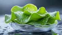 Fresh green lettuce leaf with water drops and dew in glass bowl on dark background, macro photography for food and healthy eating concepts.
