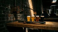 Craft beer flight with four glasses of different colored beers on wooden table against dark brick wall in pub or brewery tasting room setting.