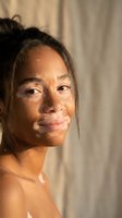 Young mixed-race woman with natural makeup-free skin in warm golden sunlight creating shadow patterns on face for skincare and beauty concepts.
