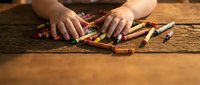 Child hands selecting colorful crayons on rustic wooden table for creative art project and drawing activities in warm natural lighting.