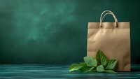 Eco-friendly kraft paper shopping bag with fresh green leaves on wooden table against dark green wall background, sustainable retail concept.
