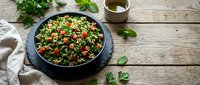 Fresh tabbouleh salad with parsley, tomatoes and bulgur wheat served in dark bowl on rustic wooden table with herbs and olive oil for healthy Mediterranean cuisine.
