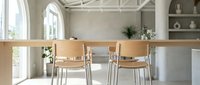 Minimalist dining room with wooden table, metal chairs, and neutral tones. Bright natural light from arched windows illuminates the clean, modern space with open shelving and potted plants for home decor.