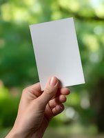 Female hand holding blank white card against blurred green natural background. Clean mockup for business card or invitation design.