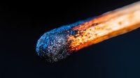 Burning match head with blue and orange flame against black background, showcasing ignition moment in dramatic macro photography.