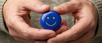 Hands gently holding blue smiley face ball symbolizing mental health support, positivity and emotional wellbeing care in protective gesture.