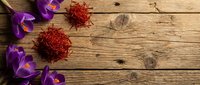 Purple crocus flowers with saffron spice threads on rustic wooden background for culinary and spring cooking concepts.