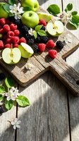 Fresh organic fruits on rustic wooden cutting board with apple blossoms. Green apples, raspberries, blackberries arranged for healthy eating and cooking.