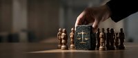 Hand placing golden scales of justice cube between wooden chess pieces on board representing legal strategy and tactical decision making in law.
