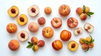 Flat lay arrangement of fresh peaches, whole and halved, displaying orange and yellow tones with red centers and green leaves on white background for food styling.