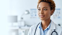 Professional African American female doctor with stethoscope smiling confidently in modern medical office setting for healthcare marketing materials.