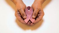 Hands gently holding pink ribbon symbol for breast cancer awareness and support campaign on white background.