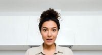 Young woman with dark curly hair in updo, olive skin tone, wearing beige collared shirt, surprised expression, isolated on white background for design use.