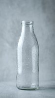 Cold glass bottle with water droplets on neutral gray background, ideal for beverage, drink, and packaging design projects.