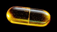 Golden transparent capsule with glittering particles inside, isolated on black background for pharmaceutical or supplement marketing.
