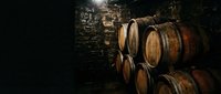 Wooden barrels stacked in a dark cellar or winery storage facility, aged oak containers for wine, whiskey, or beer production and aging process.