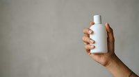 Close-up of a hand holding a white cosmetic bottle against a neutral background, suitable for skincare, beauty, and product marketing campaigns.