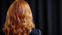 Wavy ginger hair styled in loose curls shown from behind against dark background, demonstrating professional hairstyling technique and natural red hair color result.
