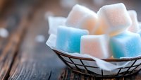 White and blue sugar cubes arranged in rustic wire basket with napkin on dark wooden table background, selective focus creates soft dreamy mood.