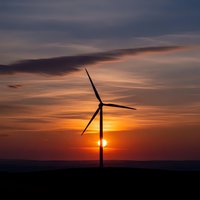 Wind turbine silhouette against dramatic sunset sky with orange and purple clouds. Renewable energy concept for sustainable power generation and environmental projects.