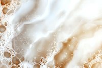 Creamy coffee and milk swirl background with frothy bubbles and soft waves creating luxurious marble effect in brown and white tones.
