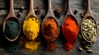 Colorful spices and herbs in wooden spoons on rustic table, including turmeric, paprika, cardamom, and spirulina powder for cooking.