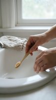 Woman holding bamboo toothbrush over white bathroom sink with natural light from window. Sustainable oral hygiene and eco-friendly dental care routine.