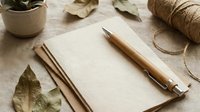 Rustic wooden pen rests on blank notebook pages surrounded by autumn leaves, twine and natural materials creating cozy writing workspace for journaling.