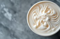Creamy swirled milk foam pattern on top of coffee drink against gray marble background, captured from above in macro photography style. Professional barista art.