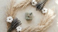 Rustic gift box surrounded by dried lavender bundles, cotton flowers and pampas grass on neutral background. Natural organic styling composition.